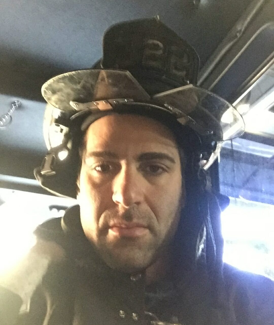 Israel Joffe wearing firefighter helmet and turnout gear in the cab of a fire truck