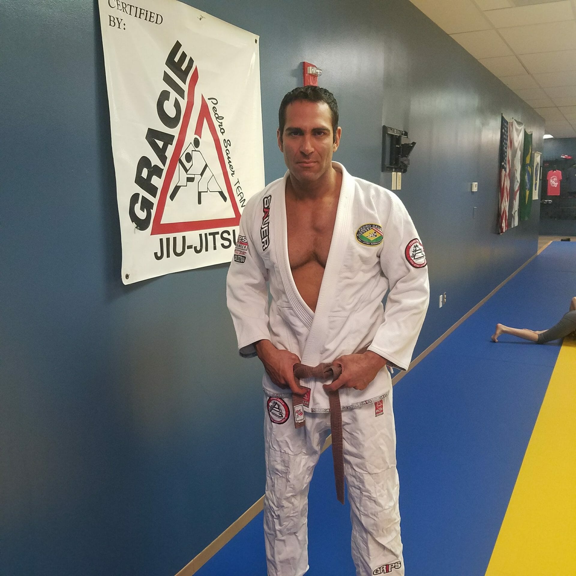 Israel Joffe in a white jiu-jitsu gi with a brown belt in front of a Gracie Jiu-Jitsu banner